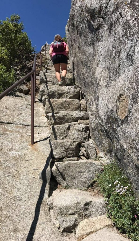 woman hiking up stone stairs granite rock on the right side